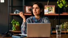 Жінка працює віддалено, тримаючи ручку і задумливо сидячи за столом