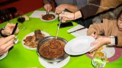 Pessoas se servem em volta de uma mesa com toalha verde para uma refeição