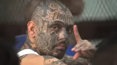 El líder de la pandilla Barrio 18, Marlon Martínez, con el rostro tatuado en el que destaca un gran 18, mira a cámara y hace gestos mientras se encuentra dentro de una celda de máxima seguridad en el tribunal Torre de Tribunales en Ciudad de Guatemala el 30 de marzo de 2011. Fue sentenciado a 47 años de prisión por el asesinato de Jorge Winter, un maestro del centro correccional Etapa II, durante un motín. FOTO AFP/Johan ORDONEZ (Foto de JOHAN ORDONEZ / AFP) (Foto de JOHAN ORDONEZ/AFP vía Getty Images)