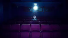 Pessoa sentada em um cinema vazio, de frente para a tela com os olhos cobertos