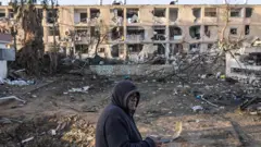 Мужчина пьет кофе, глядя на дома, разрушенные в результате ракетного удара Ирана по Димоне 22 марта 2026 года.