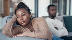 Une femme qui a l'air triste avec un homme qui croise les bras en arrière-plan