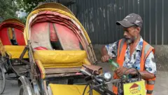 Mohammad Shukkur Ali, 50, a Bangladeshi rickshaw puller, opens a bottle of water next to his rickshaw