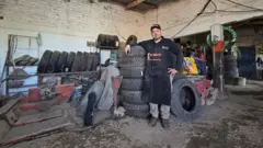 Borracheiro em uma oficina mecânica, rodeado de pneus