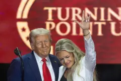 Donald Trump e Erika Trump, olhando para baixo com cara de choro e erguendo as mão esquerda para o alto, juntos no palco