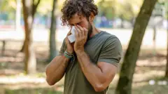 Homem limpando o nariz com papel em meio a um jardim urbano