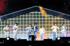 BTS no palco, usando blusas em tons pastel e calças jeans azuis