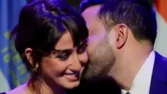 زهران ممدانی در گوش همسرش چیزی می‌گوید و هر دو لبخند می‌زنند