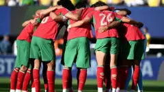 Jogadores do Marrocos, de camisas vermelhas e calções verdes, formam uma roda antes do jogo contra o Brasil pela Copa do Mundo de 2026 em Nova Jersey, nos Estados Unidos, no dia 13 de junho
