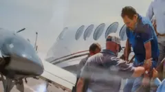 Zambadi, obučenom u plavu majicu za golf, pomažu da izađe iz malog aviona dok ga privode u julu 2024.