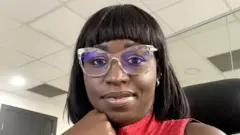 One young woman wey wear red cloth and use glasses, put hand for chin