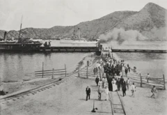 Un grupo de personas caminan por los rieles del ferrocarril y a lo lejos se ven una embarcaciones