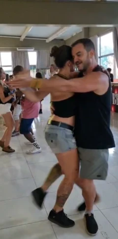 Priscila dançando forró, ela veste short jeans e blusinha preta, enquanto seu par veste uma regata preta e bermuda