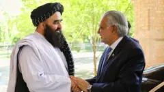 امیر خان متقی و اسحاق دار با‌هم دست داده و لبخند دارند.