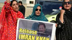পাকিস্তানের সাবেক প্রধানমন্ত্রী ইমরান খানের মুক্তির দাবির পোস্টার নিয়ে দাঁড়িয়ে আছেন তিনজন নারী