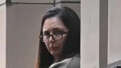 眼鏡をかけた長い髪の女性が壁越しにこちらを見ている