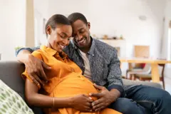 Des futurs parents assis sur un canapé, l'homme carresse le ventre de la femme