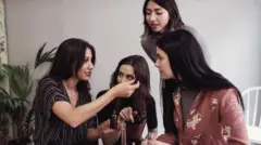 شابة بشعر أسود طويل ترتدي قميصاً بأكمام قصيرة لونه أسود ومنقط بالأبيض، تُري زميلاتها المشاركات في ورشة عمل أنبوباً يحتوي عطراً. عدد زميلاتها ثلاثة كلهن شابات ويميل لون شعرهن إلى الأسود. ترتدي واحدة منهن سترة وردية اللون بورود بيضاء، وأخرى ترتدي قميصاً يميل إلى اللون السكني والأخيرة ترتدي قميصاً قصير الأكمام بلون أسود.