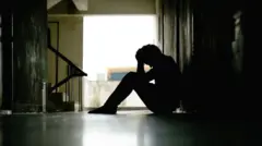 মাথায় হাত দিয়ে মেঝেতে বসে আছেন একজন, প্রতীকী ছবি