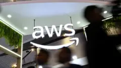 Ludzie przechodzą obok logo Amazon Web Services (AWS) na stoisku wystawcy na India Mobile Congress 2025 w Yashobhoomi, centrum konferencyjno-wystawienniczym w Nowym Delhi w Indiach