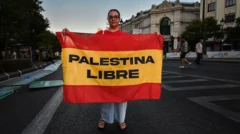 زنی وسط خیابان پرچم اسپانیا را در دست گرفته که روی آن نوشته فلسطین آزاد