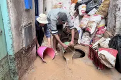 رجل بسيط يحمل جردلا من المياه ويقوم بنزح المياه المتراكمة في الشارع الضيق أمام منزله القديم وقد راكم بعضا من أكياس الرمال لحجز المياه.