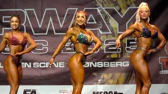 Three tanned women in bright swimsuits smile and pose, showing off their muscle definitions on stage.