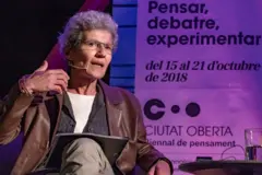 Josefina Birulés con lentes, una chaqueta marrón, sentada en una presentación pública