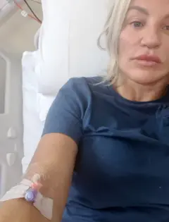 A Selfie of Joanne in the hospital, with a canula in her hand. He wears a blue Navy T -shirt. The white sheets of the hospital bed can be partially observed in the context.