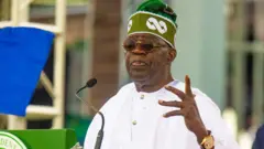 Bola Tinubu on green cap and white agbada wit im hand up