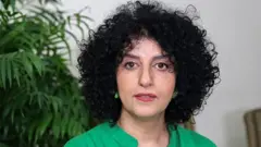 緑の服を着たイランの人権活動家モハンマディ氏が、テヘランの自宅アパートの椅子に座り、口を少し開いてカメラを見つめている