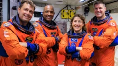 The crew in their orange flight suits standing in what looks like an Orion training room all smiling and with their arms folded