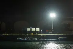 Una imagen de noche de un sumergible en el agua mientras varias personas están descargándolo en un puerto de concreto.