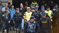 काठमाण्डू जिल्ला अदालतअगाडि प्रहरीले घेरिएका दुर्गा प्रसाई र उनका अङ्गरक्षक भनिएका दीपक खड्का 