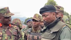 Iburyo; Gen Jeff Nyagah ukuriye ibikorwa by'ingabo za EAC ziri muri Congo na Maj Willy Ngoma umuvugizi wa gisirikare wa M23 mu gikorwa cyo guha izo ngabo agace ka Kibumba mu kwezi gushize