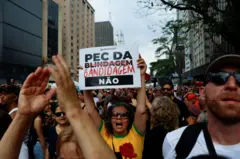 Protesto contra PEC da Blindagem na Avenida Paulista, no domingo (21/09). No centro, no meio de uma multidão, está uma mulher usando camiseta amarela da seleção brasileira segurando um cartaz 'Pec da Blindagem Não', com a palavra Blindagem riscada e substituída por 'Bandidagem'