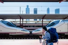 Uma mulher de mochila caminhando pela plataforma de uma estação, onde um trem de alta velocidade está parado