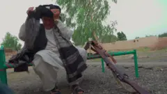 Ҳукмина ўриндиқда бошига салла ўраяпти, ёнида милтиғи турибди