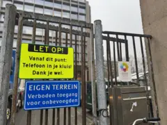 Metallzäune rund um eine Schule mit leuchtend gelben Schildern, die die Schüler dazu auffordern, ihre Telefone in Schließfächern zu lassen