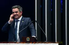 Ciro, de terno, fala ao celular e sorri, da tribuna do Senado Federal