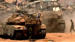 Izraelski tenkovi na prašnjavom terenu dok vojnici hodaju okolo 