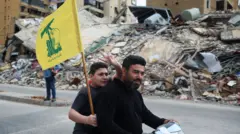 Una persona sostiene una bandera de Hezbolá al pasar junto a un edificio dañado, después de que entrara en vigor un alto el fuego de 10 días entre el Líbano e Israel