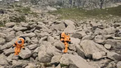 Duas pessoas vestidas com trajes de astronauta laranja sobre rochas nos Alpes suíços