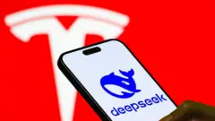 Mão sustenta um telefone celular, em cuja tela se observa o logotipo da Deepseek. Ao fundo, se observa o logotipo da Tesla.