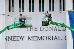 Dos operarios subidos a máquinas para trabajar frente a la fachada del Centro Kennedy, que muestra el nombre de Trump encima del de Kennedy.