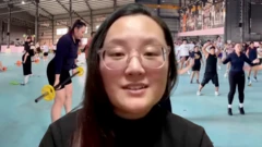TL Huang looks at the camera in a headshot that is cut off from the shoulders. She wears glasses and has long black hair. Behind her, pictures from the camp she attended have been edited - they feature tens of attendees lifting weights and doing aerobic exercise in a huge hall.
