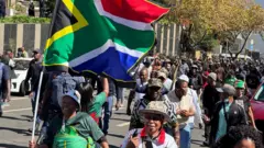 Woman hold South Africa flag wit oda women for di background