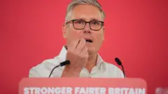 Starmer za govornicom ispred koje je tabla na kojoj je slogan: 'Jača i poštenija Britanija'