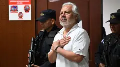 O advogado constitucionalista Enrique Anaya, escoltado por dois policiais armados, chegando para audiência em 24 de junho de 2025