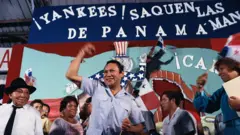 Manuel Antonio Noriega delante de una pancarta que dice "Yankees saquen las manos de Panamá"